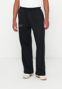 Μαύρες φόρμες από μαλακό ύφασμα, με ελαστική μέση και κορδόνι ρυθμιστή, με λογότυπο τυπωμένο στον αριστερό μηρό.