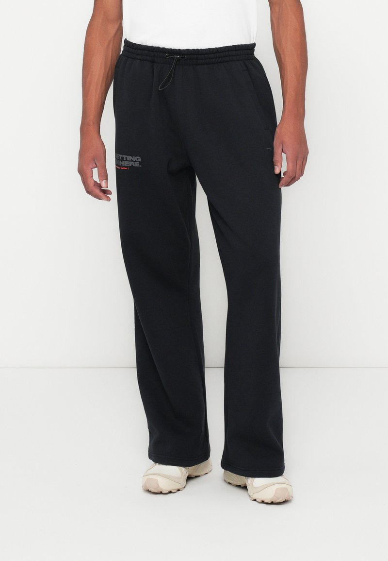 Μαύρες φόρμες από μαλακό ύφασμα, με ελαστική μέση και κορδόνι ρυθμιστή, με λογότυπο τυπωμένο στον αριστερό μηρό.