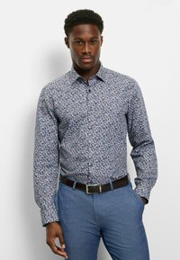 Langärmliges Hemd mit floralem Muster auf blauem Hintergrund, mit mehrfarbigen Blattmustern, einem normalen Kragen und einer geknöpften Vorderseite. Kombiniert mit hellblauen Hosen.