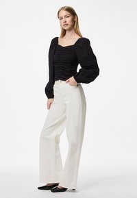 Blusa nera arricciata con maniche a palloncino abbinata a pantaloni bianchi a vita alta e gamba larga, con ballerine nere appuntite. Design semplice, colori neutri.