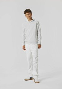 Felpa grigia con tasca a canguro abbinata a jeans bianchi e sneakers bianche con dettagli neri. Design semplice e tessuto morbido.