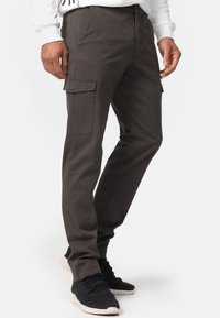 Grå cargo-byxor med sidofickor, tapered fit, tillverkade av en bomullsmix. Bärs med svarta sneakers, vilket visar en mjuk textur.