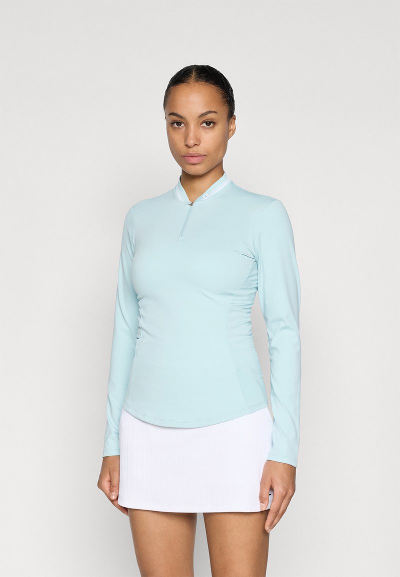 Světle modrý dlouhý rukáv sportovní top s polozipem, hladkou texturou a přiléhavým střihem, spárovaný s bílou skládací sukní.