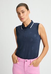 Polo shirt senza maniche di colore blu navy con colletto bianco, caratterizzato da un design a motivo sottile. Il modello indossa pantaloni rosa, con le mani in tasca.