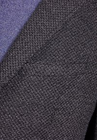 Tessuto nero strutturato combinato con un materiale blu liscio, caratterizzato da un motivo sottile, che mostra un contrasto tattile e elementi di design a strati.