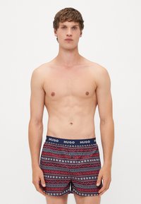Boxeri cu o talie elastică albastră marină, având logo-ul "HUGO". Design cu model în dungi roșii și albe, cu accente geometrice.