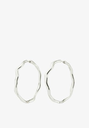 Par srebrne naušnice u obliku nepravilnih obruča s glatkim, valovitim rubovima i zatvaranjem na zaklopku na bijeloj pozadini.