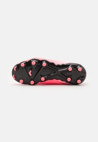 Botte de football avec un dessus synthétique rose et une semelle en caoutchouc noire, dotée de plusieurs crampons moulés roses pour une meilleure traction.