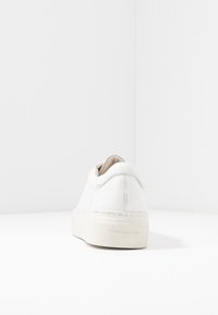Adidași din piele albă, cu o formă rotunjită, talpă plată și detalii delicate de cusătur�ă. Include un interior de culoare crem și un călcâi cu branding.