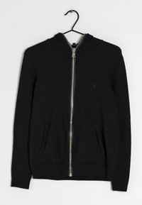 Sort zip-up hoodie med to forlommer, ribbede manchetter og kant, hængende på en sort bøjle mod en hvid baggrund.