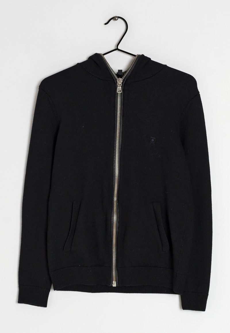 Sort zip-up hoodie med to forlommer, ribbede manchetter og kant, hængende på en sort bøjle mod en hvid baggrund.