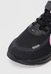 Chaussure de sport noire avec un dessus en maille texturée, des accents roses et une semelle en caoutchouc avec un motif de tôle distinct. Les lacets sont noirs.