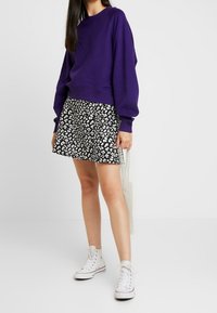 Lila Sweatshirt mit langen Ärmeln, kombiniert mit einem schwarzen Rock mit weißem Leopardenmuster. Weiße High-Top-Sneaker runden das Outfit ab.