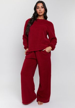Conjunto de loungewear acogedor de forro polar rojo que incluye un suéter de corte holgado con cuello redondo y pantalones de pierna ancha con bolsillos laterales. Superficie texturizada.