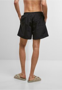 Sorte svømmedragtshorts med en let tekstur, elastisk talje og sidelommer. Båret med lyse slides med præget logo.