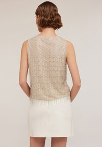 Beige mouwloos top met een textuur van sequins, voorzien van een geschulpte rand en franjes aan de onderkant, getoond vanaf de achterkant.