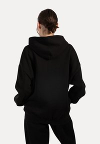 Czarna, oversize bluza z kapturem, wykonana z miękkiego materiału, z dużym kapturem i ściągaczami na rękawach. Posiada luźny krój i minimalistyczny design.