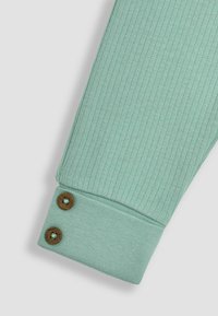 Tissu côtelé vert menthe avec une manchette comportant deux boutons marron. La manchette a une texture lisse, contrastant avec le matériau côtelé au-dessus.