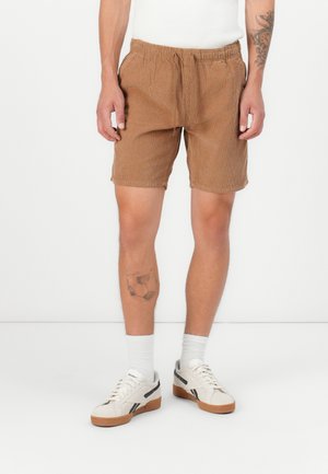 Shorts en velours côtelé marron avec une taille élastique et un cordon de serrage, offrant une coupe décontractée et des poches latérales, associés à des baskets blanches.