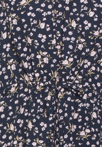 Vestito floreale con uno sfondo blu scuro, piccoli fiori rosa e gialli, vita arricciata e dettaglio con fiocco per la regolazione.