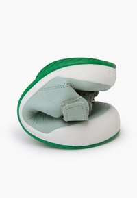 Zapato de cuero verde claro con una suela texturizada blanca y verde, que cuenta con una correa de velcro y un diseño enrollado y flexible.
