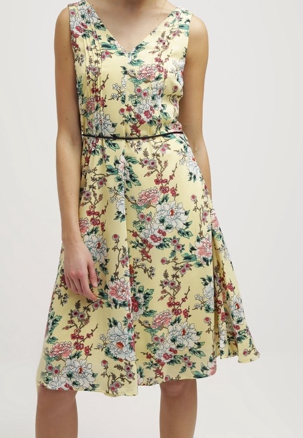 Robe fleurie avec un décolleté en V, tissu jaune ornée de motifs floraux roses et verts, plis aux épaules, et taille ajustée.