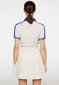 Pikétröja i ljusgrått med blå detaljer, med ribbad krage och korta ärmar. Matchad med en veckad beige kjol.