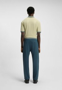 Polo shirt in light beige with contrasting collar and sleeve stripes, paired with dark teal trousers. Smooth fabric with a relaxed fit.