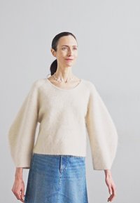 Κρέμα πουλόβερ από μαλλί με υπερμεγέθη μπαλονί σ sleeves, συνδυασμένο με μπλε τζιν φούστα. Μαλακή υφή, στρογγυλή λαιμόκοψη και άνετη εφαρμογή.