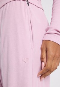 Light pink ribbed joggers with a side pocket and a small embroidered logo. Soft texture with a fitted design and elastic waistband.