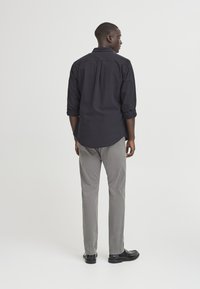 Black button-up shirt with rolled sleeves, paired with light gray pants and black shoes. The fabric appears smooth and casual.