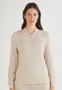 Beżowy sweter prążkowany z dekoltem w kształcie litery V, długimi r�ękawami i miękką fakturą. Kołnierz ma jaśniejszy odcień, co uzupełnia ogólny design.