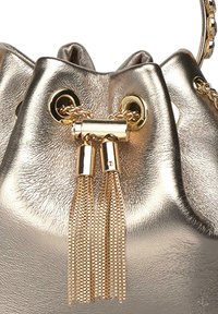 Bolsa de mano tipo bucket en un tono dorado metálico con acabado de cuero texturizado, que presenta herrajes en tono dorado, cierre de cordón y acentos de cadena con borlas.