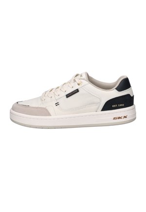 Baskets basses beige avec semelle blanche, panneau noir au talon marqué « EST. 1992 » et petite étiquette « Skechers » sur le côté.