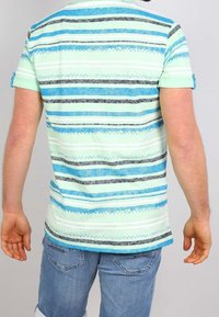 Camisa de manga corta en verde claro con rayas horizontales en azul, negro y blanco. Presenta un patrón texturizado y mangas enrolladas.