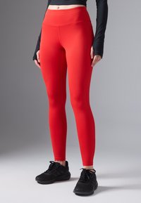 Lysende røde tights med høy midje, glatt tekstur og minimale sømmer. Brukt sammen med svarte treningssko med strukturelle detaljer.