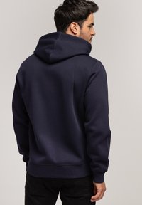 Granatowy hoodie z teksturowanego materiału, z przednią kieszenią kangurką, kapturem na sznurku i ściągaczami przy rękawach. Zaprojektowany w luźnym fasonie.