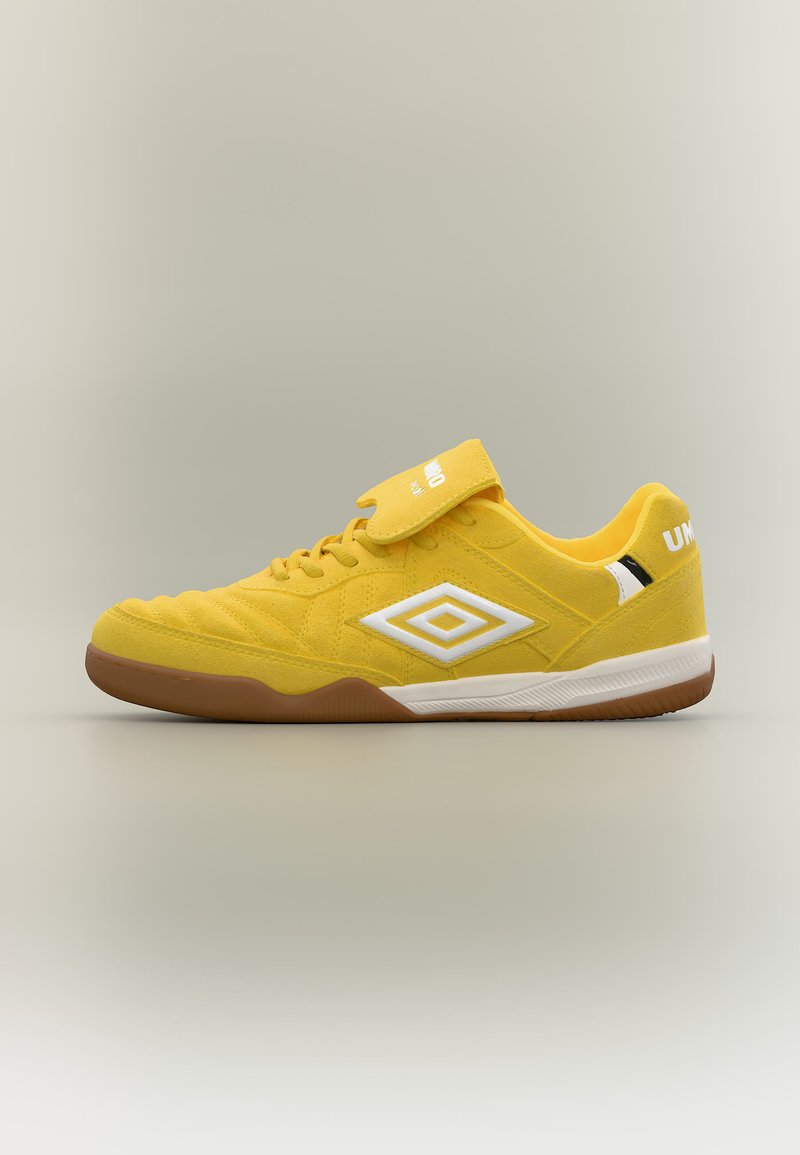 Κίτρινο παπούτσι για εσωτερικό ποδόσφαιρο Umbro με λευκό λογότυπο, λαστιχένια σόλα και αυτοκόλλητο ιμάντα πάνω από τα κορδόνια σε ουδέτερο φόντο.