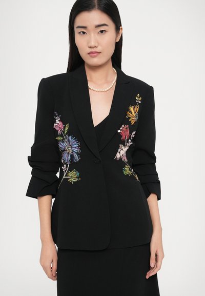 Fekete blézer színes virágos hímzéssel, strukturált hajtókával és pliszírozott ujjakkal. Sima anyag, szabott illeszkedés és egyetlen gombos záródás.