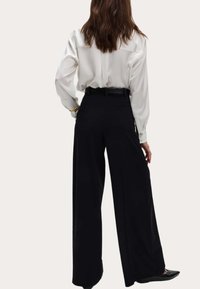 Pantalones negros de pierna ancha con una textura suave, complementados por una blusa blanca de seda de manga larga; diseño liso con cintura ajustada y cinturón.