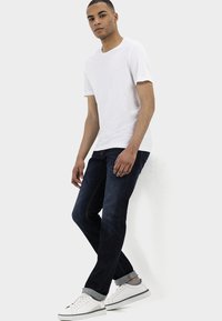 Witte T-shirt met korte mouwen, donkere denim jeans en witte sneakers. De jeans hebben een rechte snit; de sneakers hebben grijze accenten en een subtiel ontwerp.