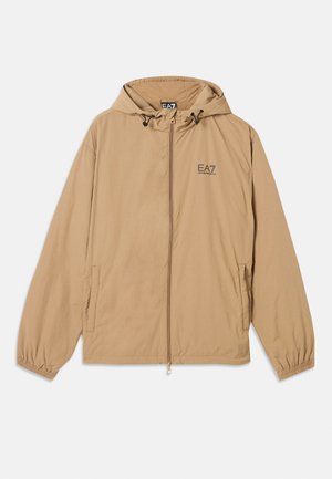 Svijetlosmeđi kaput s kapuljačom napravljen od mekanog materijala, s prednjim patentnim zatvaračem, elastičnim manžetama i logotipom na lijevoj strani prsnog dijela. Ima dva bočna džepa.