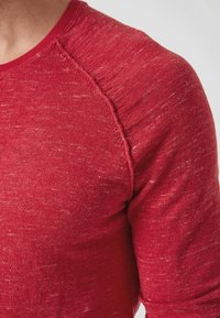 Maglietta a manica lunga in maglia rossa, testurizzata, con scollatura rotonda e maniche raglan. Le sottili variazioni di colore creano un aspetto melange.