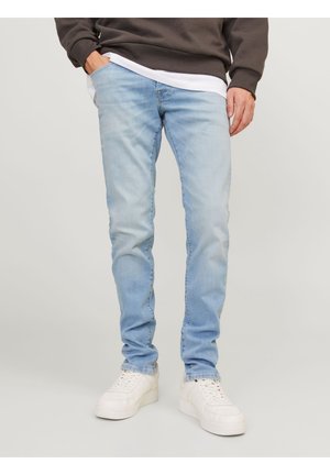 Jeans de mezclilla de color azul claro con un ajuste slim, costuras visibles y ligero desgaste. Combinados con zapatillas blancas y un sudadera gris.