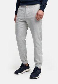 Chinos gris claro con un corte ajustado, que cuentan con un puño elástico y bolsillos frontales, combinados con zapatillas azul oscuro con suelas blancas.