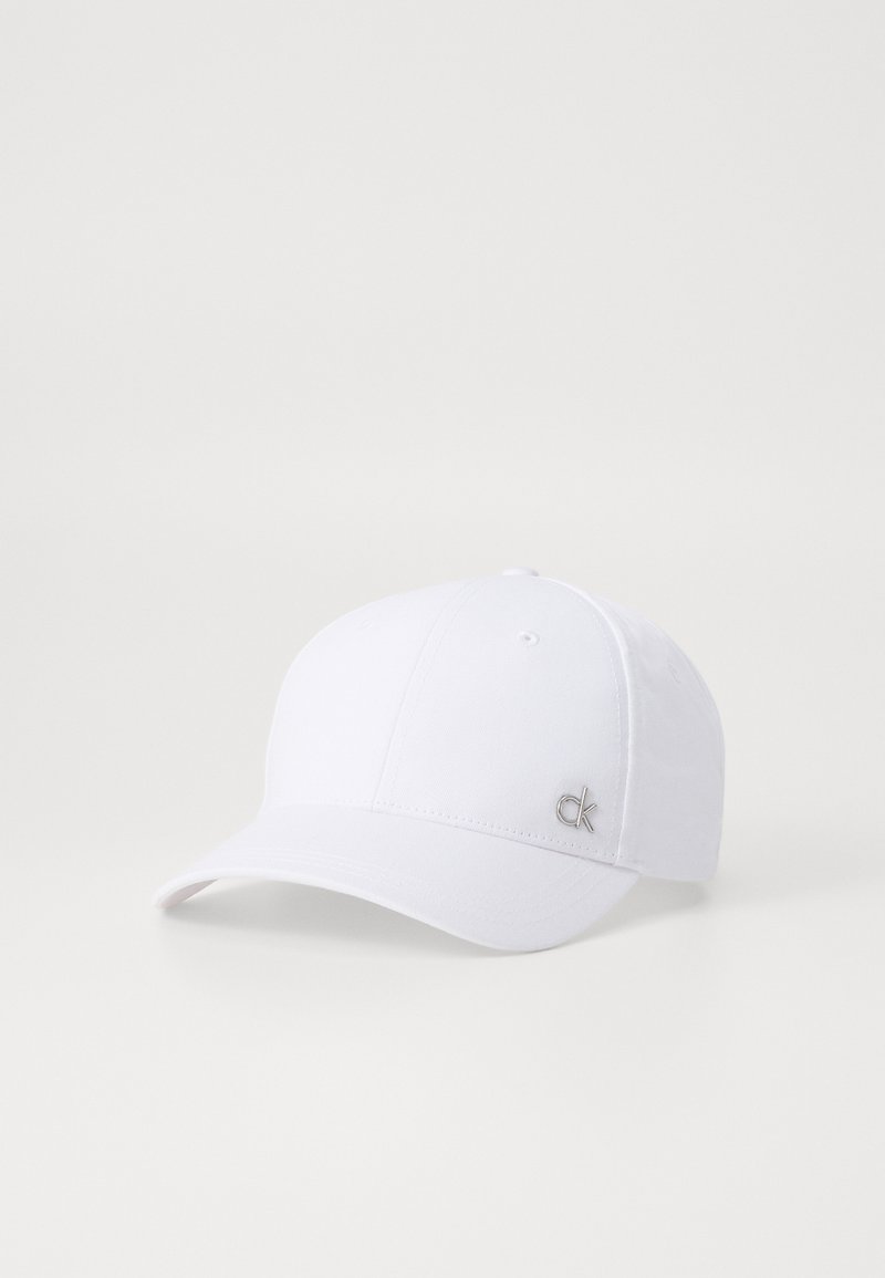 Hvit baseballcaps laget av bomull med rund krone, buet visir og en liten sølvfarget "ck"-logo på siden.