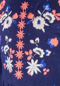 Námořnická tkanina s komplikovanou květinovou výšivkou v růžové, bílé a modré. Mezi charakteristiky patří vrstvené textury a podrobné vzory šití.