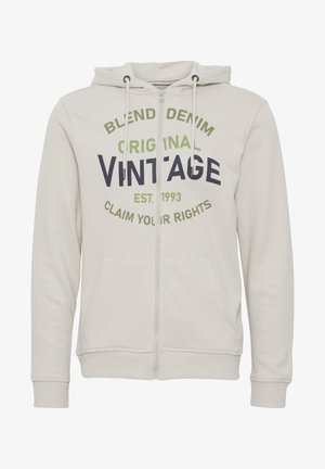 Lys grå zip-up hettegenser laget av mykt stoff med kengurulomme. Har svart og grønn tekst: "BLEND DENIM ORIGINAL VINTAGE" på forsiden.