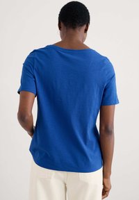 Rövid ujjú, laza fitneszű kék póló, kerek nyakkivágással és sima textúrával, világos színű nadrággal párosítva.