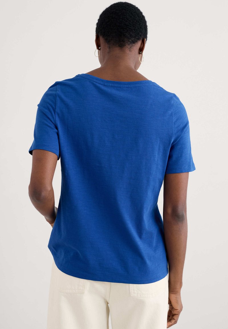 Rövid ujjú, laza fitneszű kék póló, kerek nyakkivágással és sima textúrával, világos színű nadrággal párosítva.